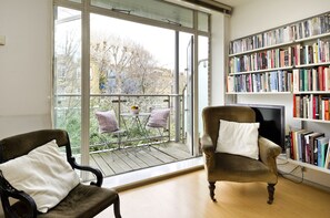 A room with a large window, a bookshelf, a television, and two chairs.