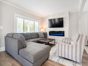 Un salon moderne avec un canapé d’angle, une table basse, un fauteuil à rayures, une cheminée et un téléviseur fixé au mur.
