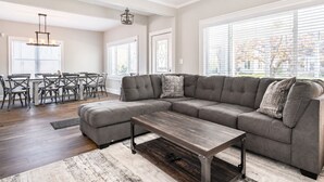 A spacious living room with a sectional sofa, a coffee table, and a dining area with a table and chairs. - New Remodel with Hot Tub 3 blocks from Beach, 1 block to Town, & Game Room! (South Haven)