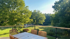 A wooden deck with a table and chairs, overlooking a grassy area with trees. - NEW LISTING: Large Creemore farmhouse on 50 acres with Tennis and Pool (Honeywood)