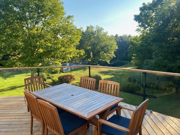A wooden deck with a table and chairs, overlooking a grassy area with trees.
