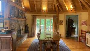 A dining area with a wooden table and chairs, a stone wall, and a view through large windows. - NEW LISTING: Large Creemore farmhouse on 50 acres with Tennis and Pool (Honeywood)