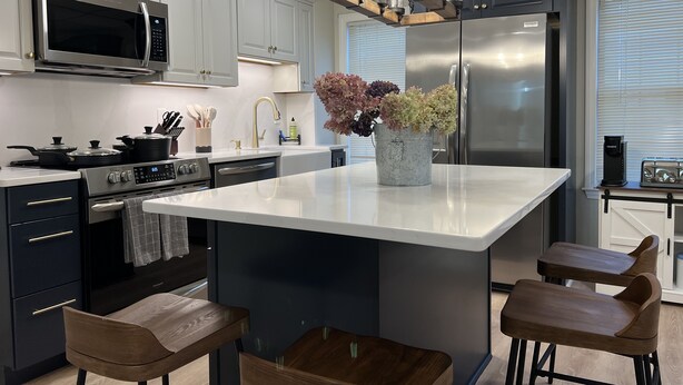 Een moderne keuken met een centraal eiland, roestvrijstalen apparatuur en houten barkrukken.