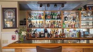 Un espace bar avec des étagères remplies de bouteilles d’alcool et de verres, un comptoir en bois et un détecteur d’incendie au mur.