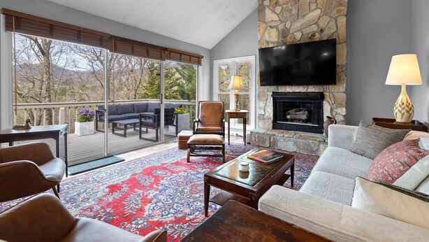 A spacious living room with a stone fireplace, a flat-screen TV, and a balcony with outdoor furniture. - Family and Pet Friendly Mountain Home with a view.  No Hurricane Damage (Pisgah Forest)