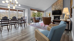 A spacious living room with a dining area, a stone fireplace, and a large window overlooking a deck. - Family and Pet Friendly Mountain Home with a view.  No Hurricane Damage (Pisgah Forest)