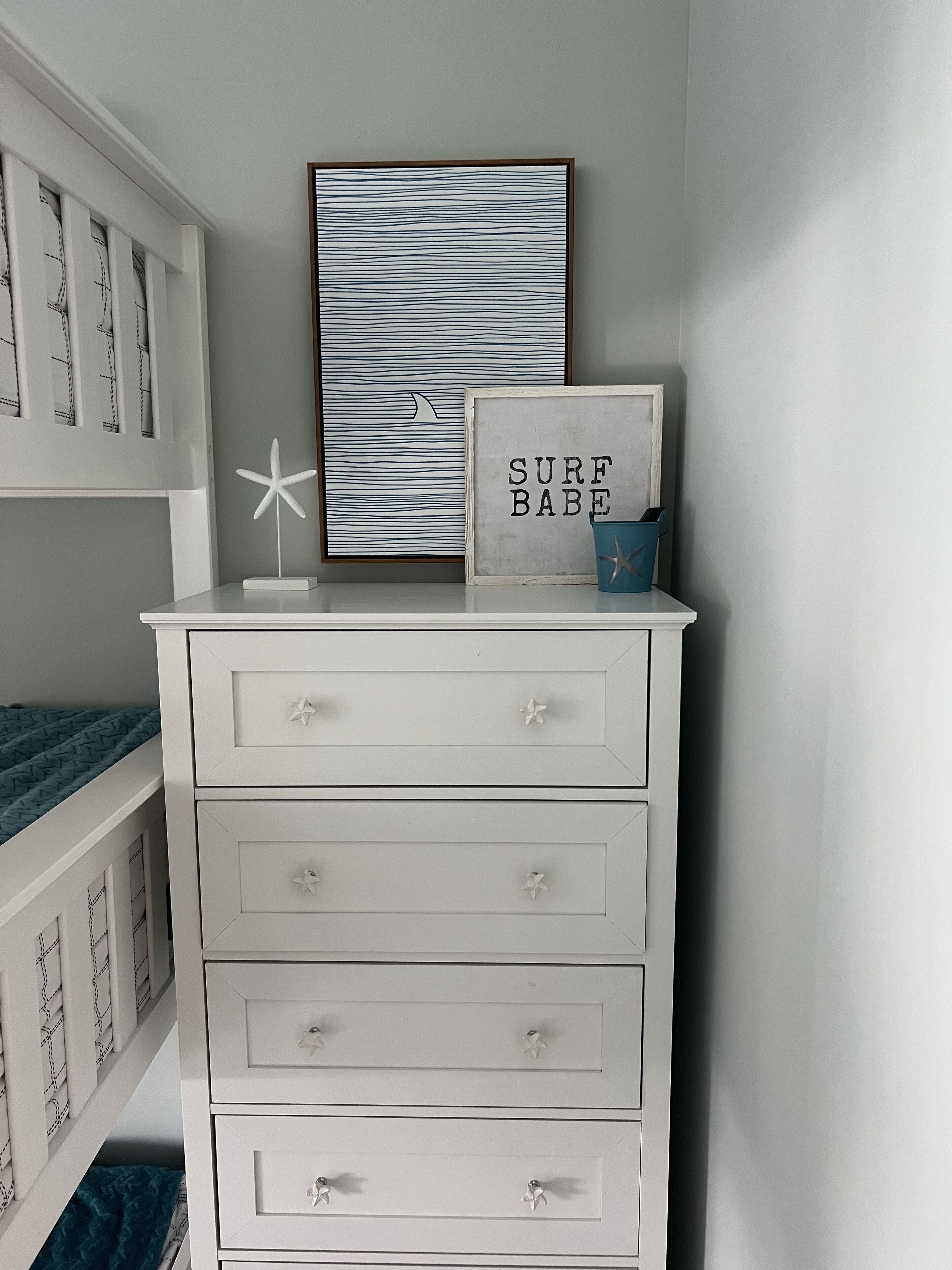 A white dresser with drawers, a framed picture with the text "SURF BABE" and a starfish decoration.