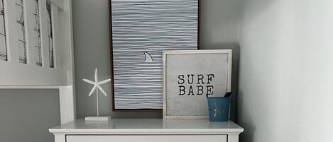 A white dresser with drawers, a framed picture with the text "SURF BABE" and a starfish decoration.