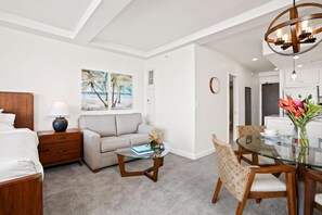 Una habitación de hotel moderna con cama, sofá, mesa de centro de vidrio, mesa de comedor con sillas y obras de arte en las paredes.