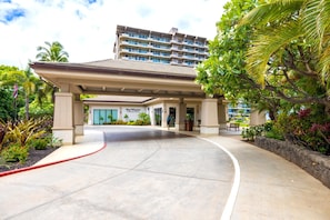 A hotel entrance with a covered walkway, palm trees, and a building with multiple balconies.