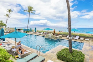 A pool area with lounge chairs, umbrellas, and a view of the ocean.