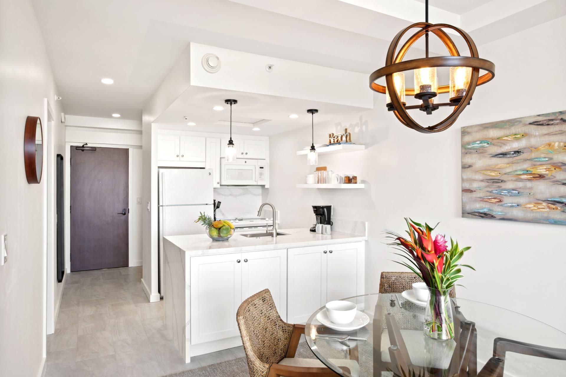 A modern kitchen with white cabinets, a central island, and a dining area with a glass table and wicker chairs.