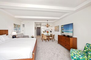 Ein modernes Hotelzimmer mit einem großen Bett, einem Essbereich, einem Fernseher und Blick auf den Strand.