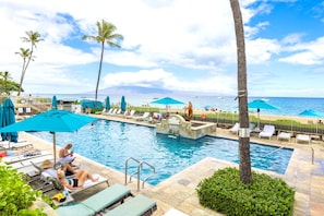 A pool area with lounge chairs and umbrellas, a lifebuoy, and a view of the ocean.