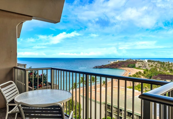 A balcony with a table and chairs, overlooking a beach and ocean.