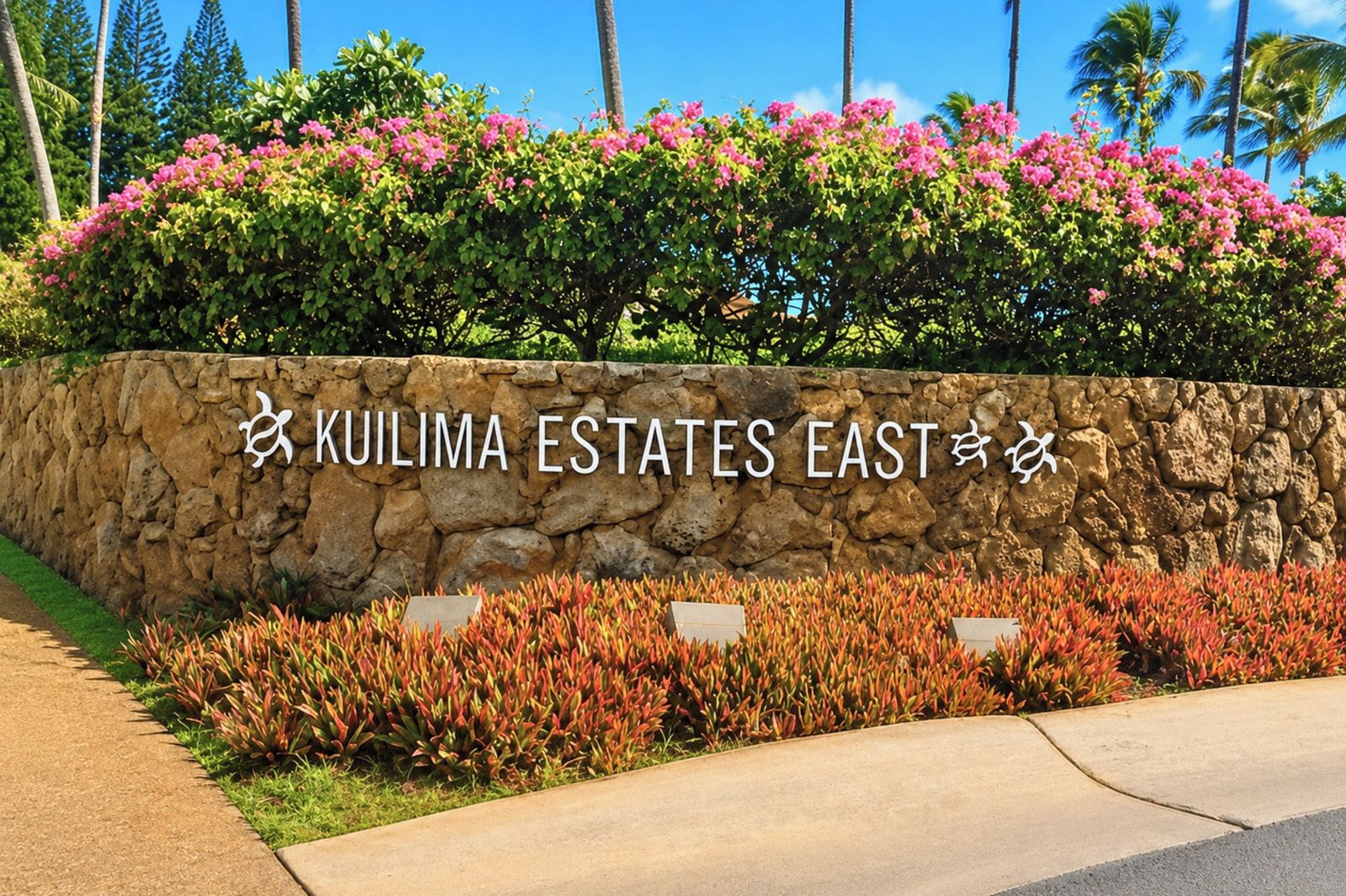 A stone wall with 'KULIMA ESTATES EAST' signage, surrounded by lush greenery and pink flowers.