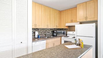 A compact kitchen with wooden cabinets, a microwave, a stove, and a refrigerator.