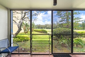 Une pièce dotée d’une grande porte-fenêtre coulissante donnant sur un jardin où se trouvent un banc et une chaise.