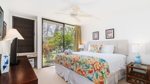 Habitación de hotel con cama, escritorio, televisor, ventilador de techo y una ventana grande.
