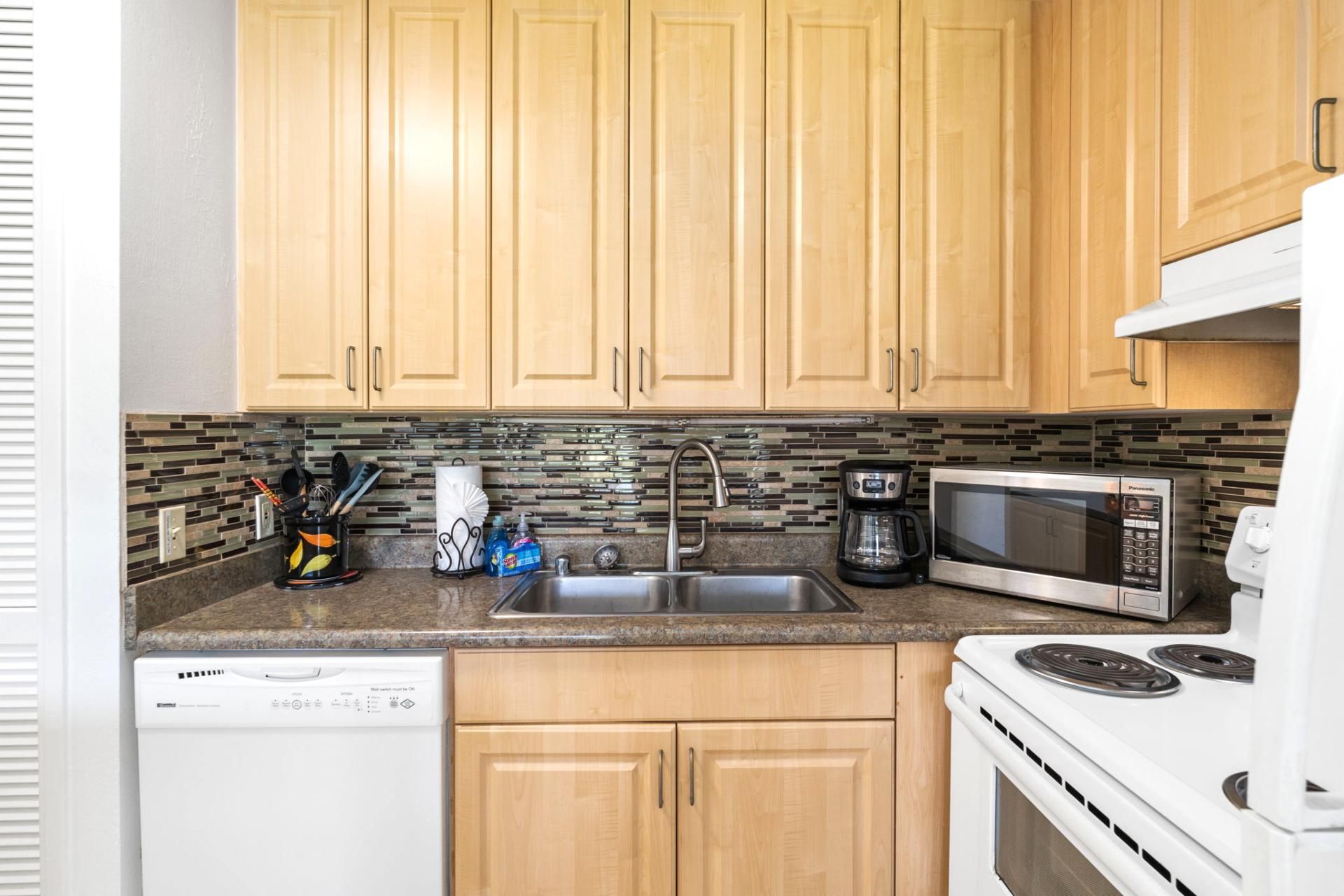 A compact kitchen with wooden cabinets, a stainless steel sink, a microwave, a coffee maker, and a dishwasher.