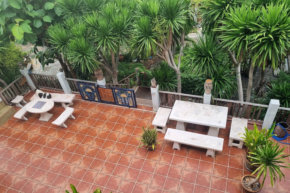 Eine Terrasse mit Fliesenboden, weißen Bänken und einem Tisch mit blau-weißer Musterung.