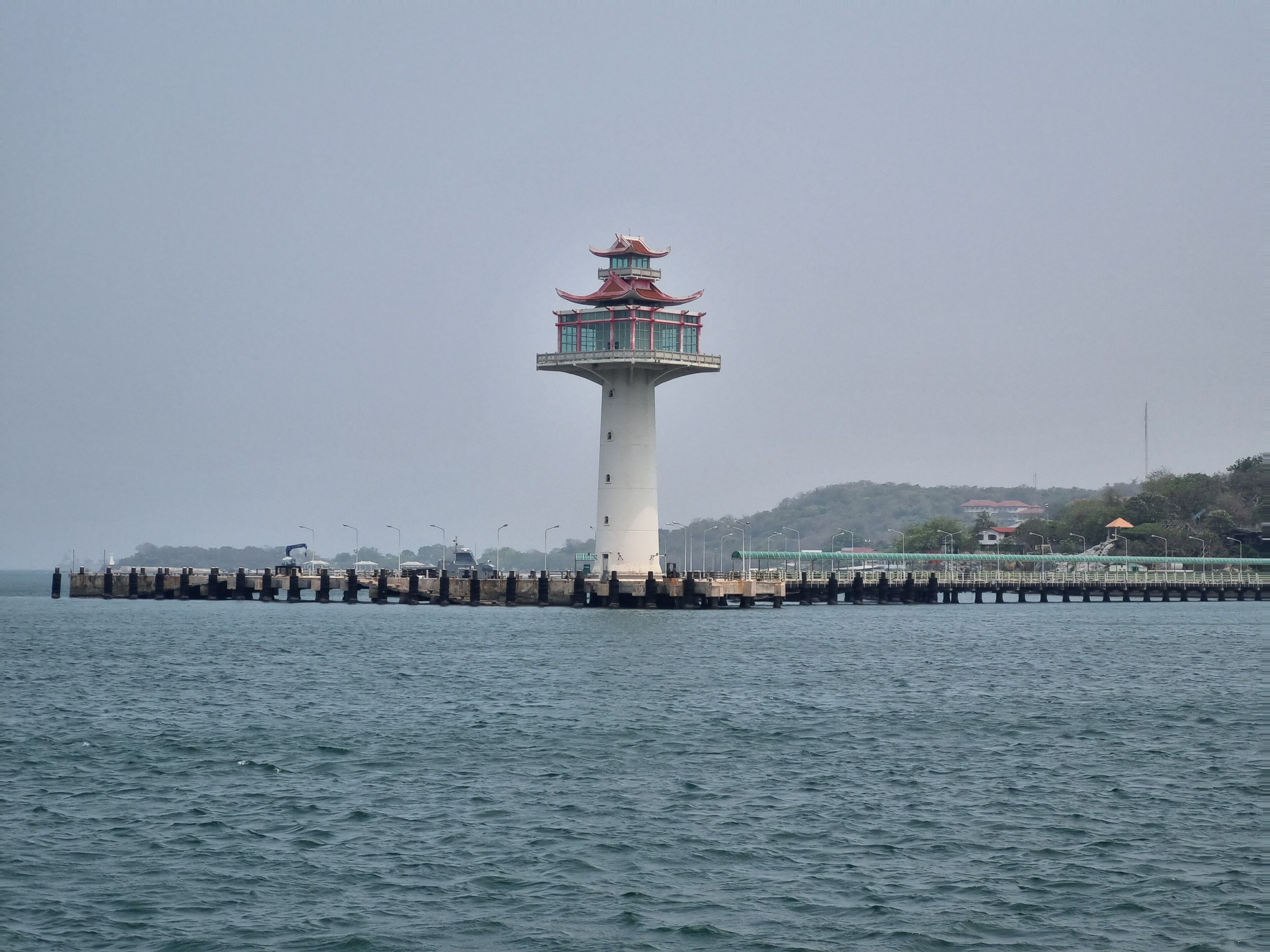A lighthouse with a traditional design, situated at the end of a pier extending into the water.