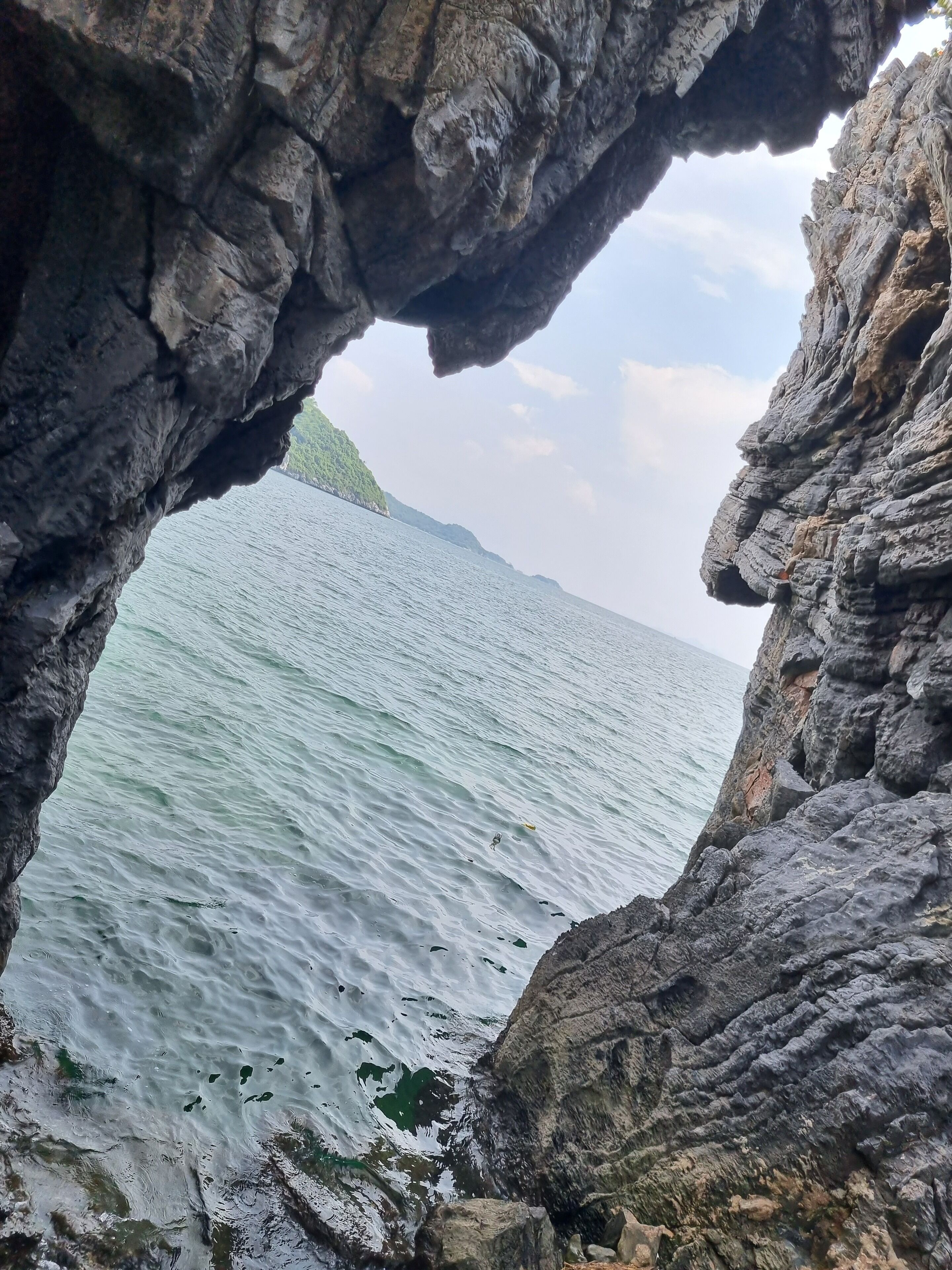 Formação rochosa natural com vista para o mar e uma colina verde distante.