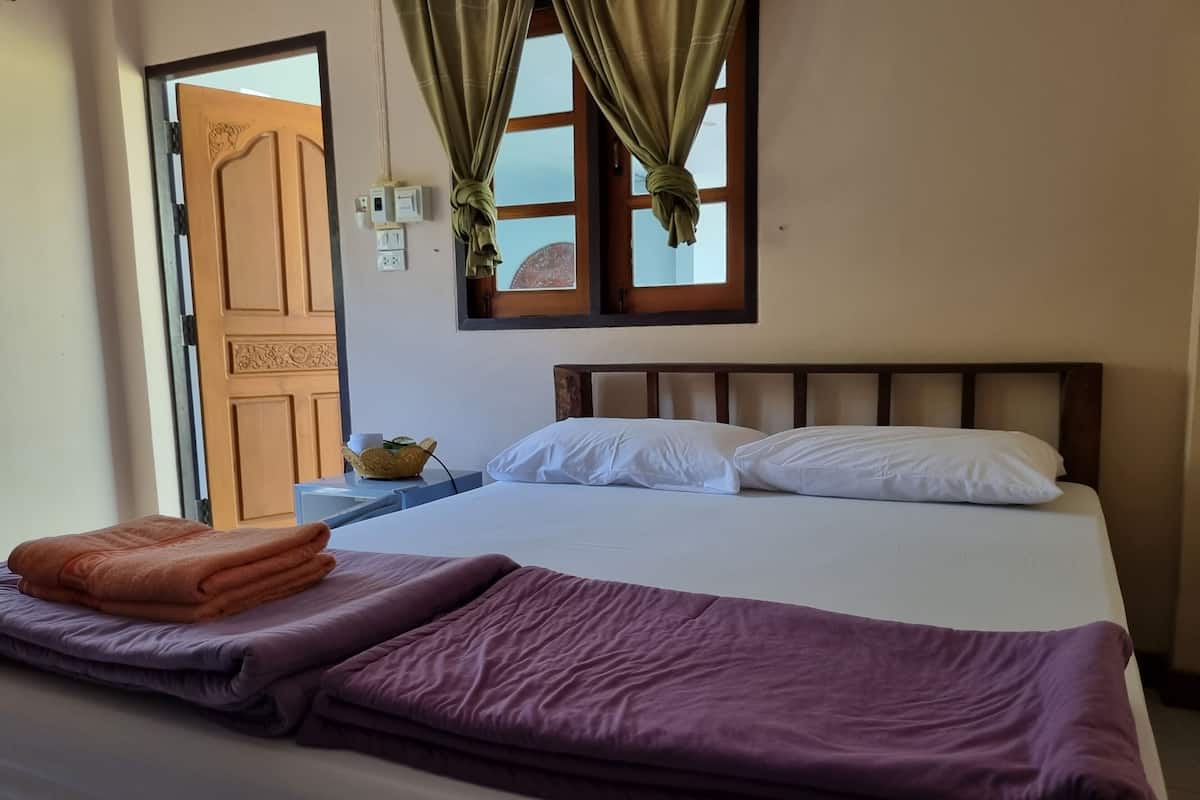 Ein Bett mit weißen Kissen, einer violetten Decke und einem orangefarbenen Handtuch.