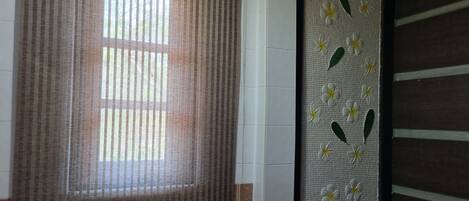 A bathroom with a window covered by a striped curtain, a white sink, and a decorative panel with flowers and leaves.