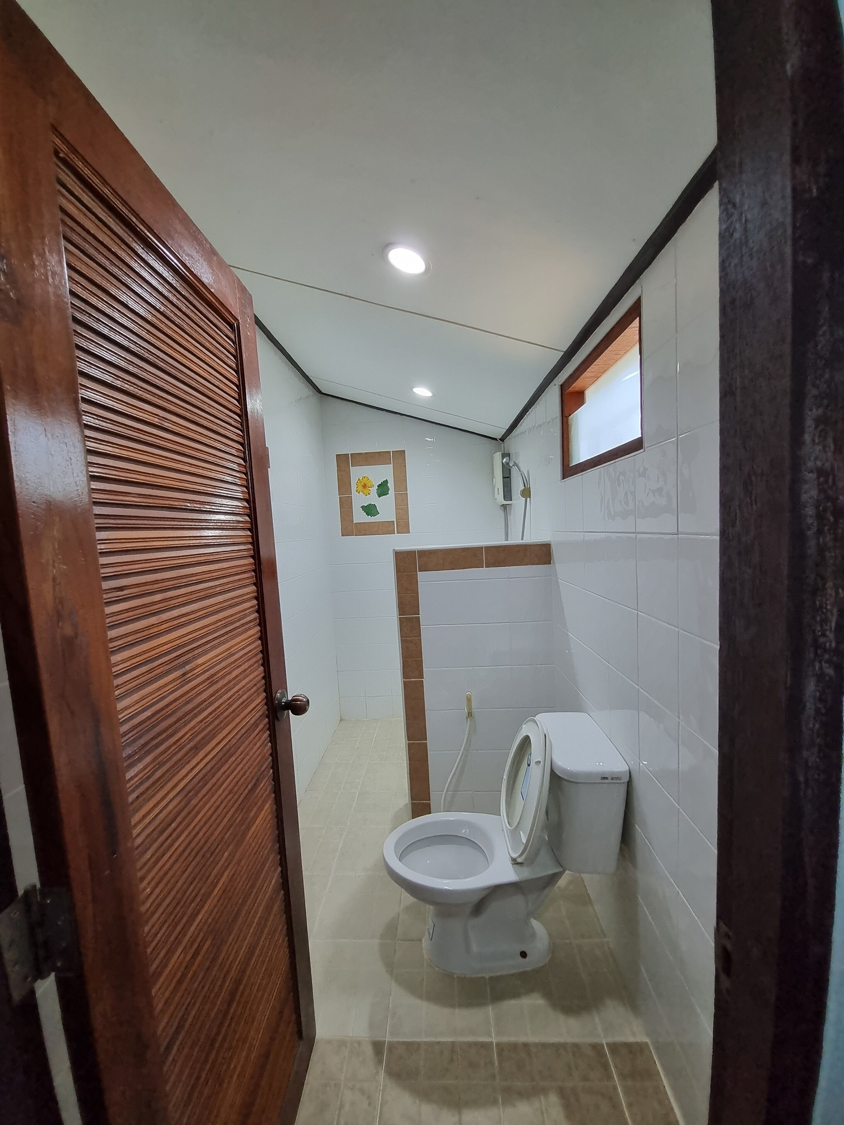 Une petite salle de bain avec des toilettes, une douche et une porte en bois.