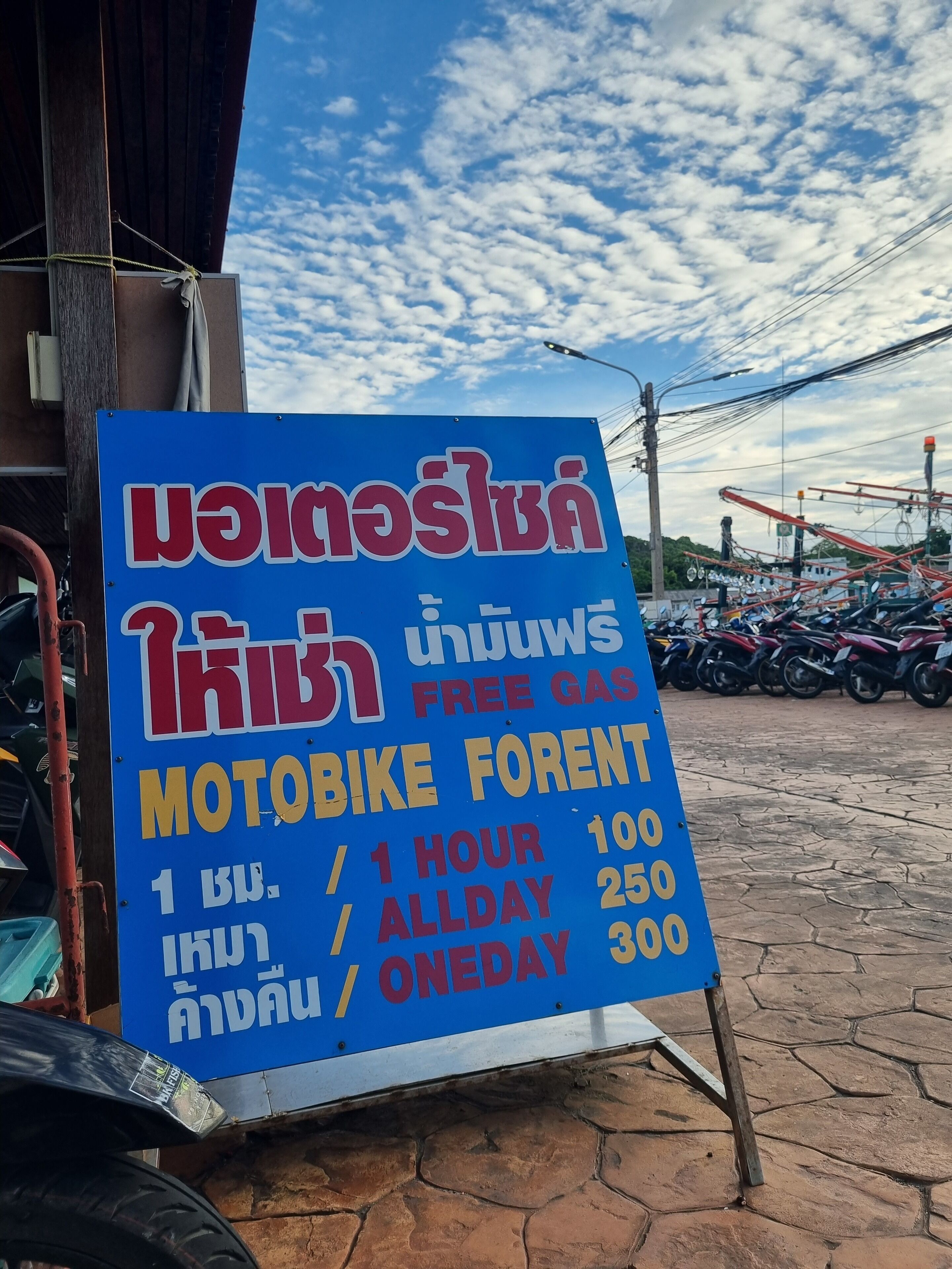 A blue sign advertising a motorbike rental service with rates for 1 hour, all day, and one day rentals.