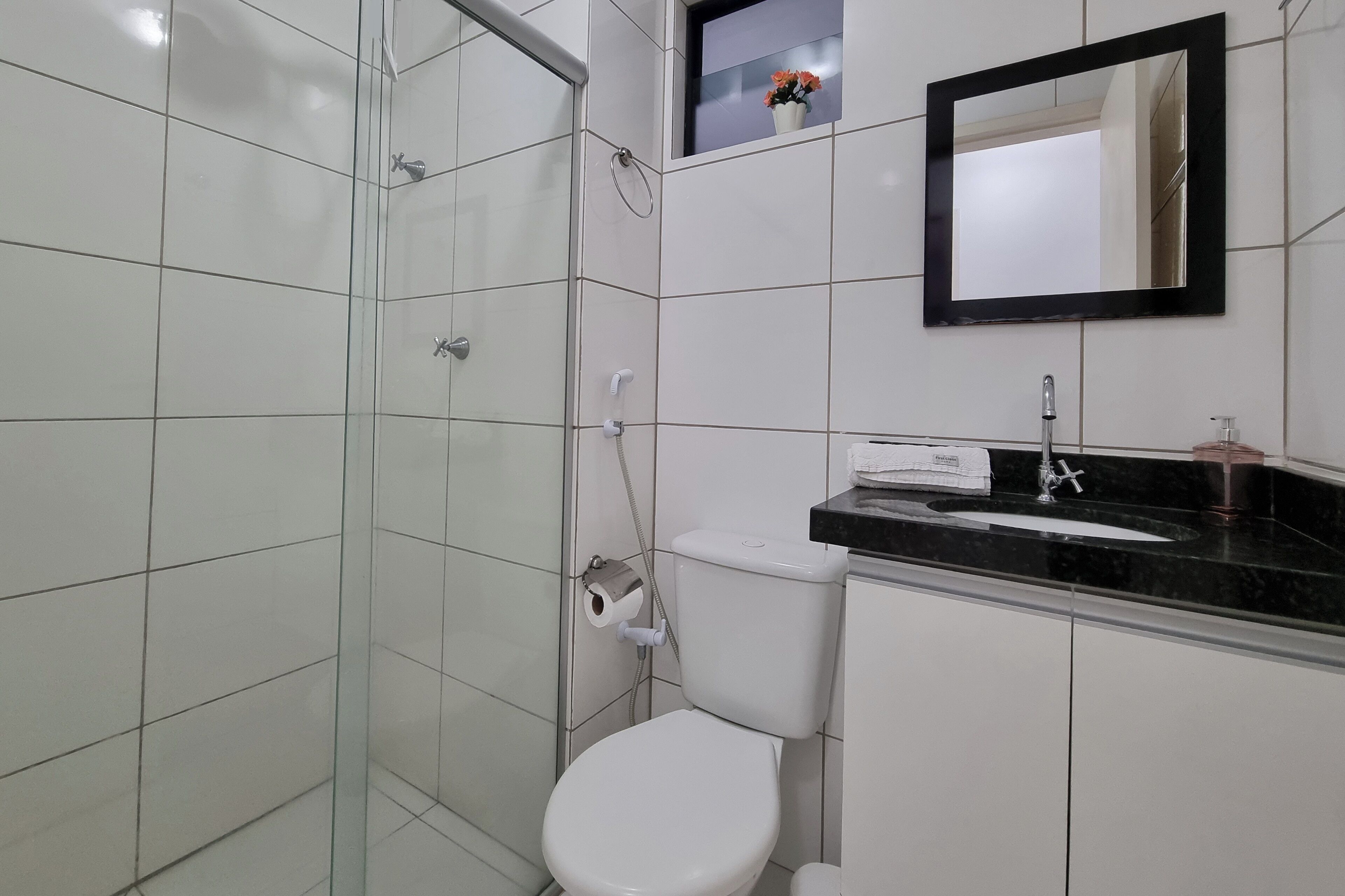 A bathroom with a glass-enclosed shower, a white toilet, a black countertop sink, and a mirror above it.