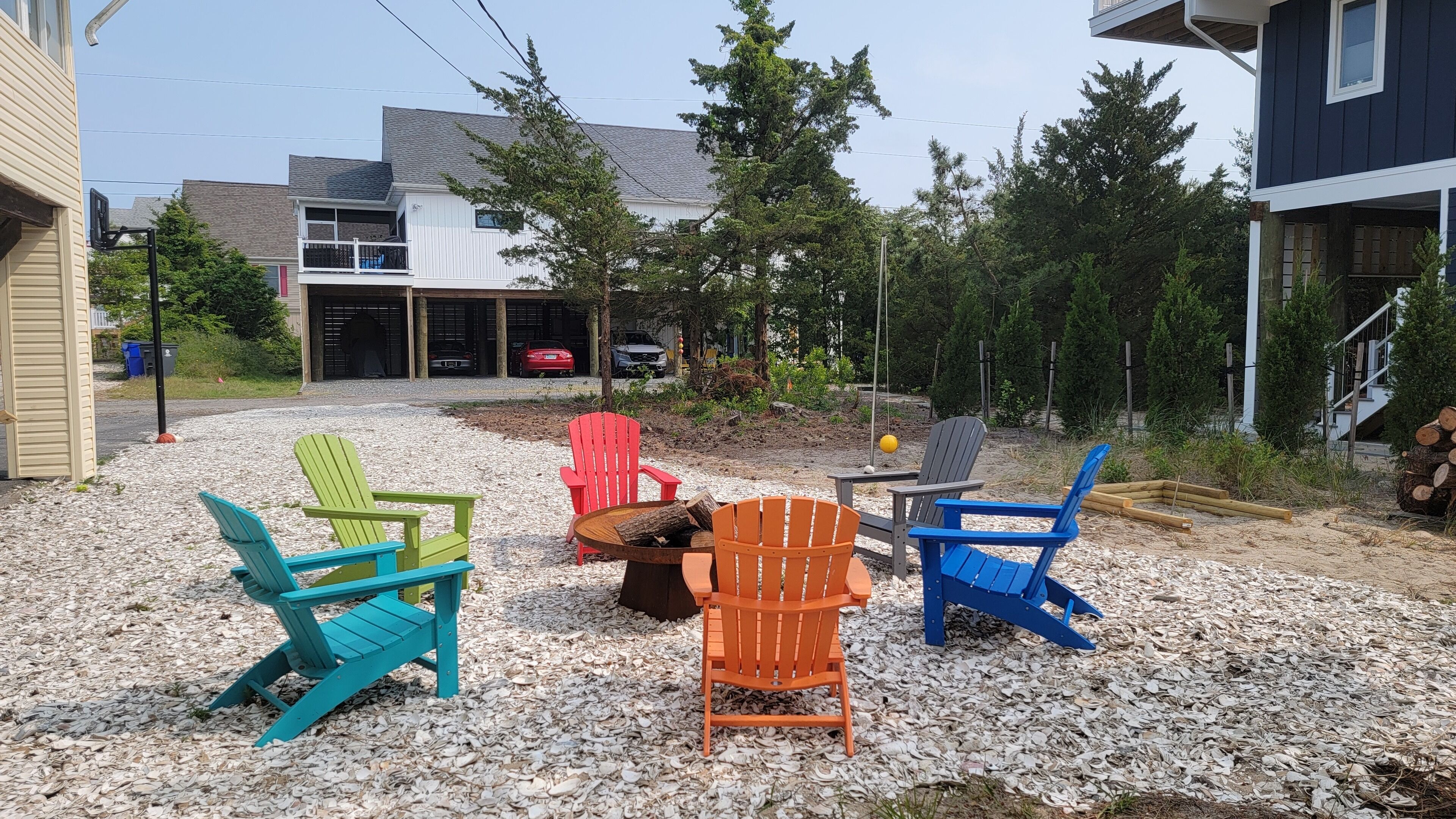 Un espace extérieur aménagé avec des chaises Adirondack aux couleurs vives, un foyer et un sol en gravier.