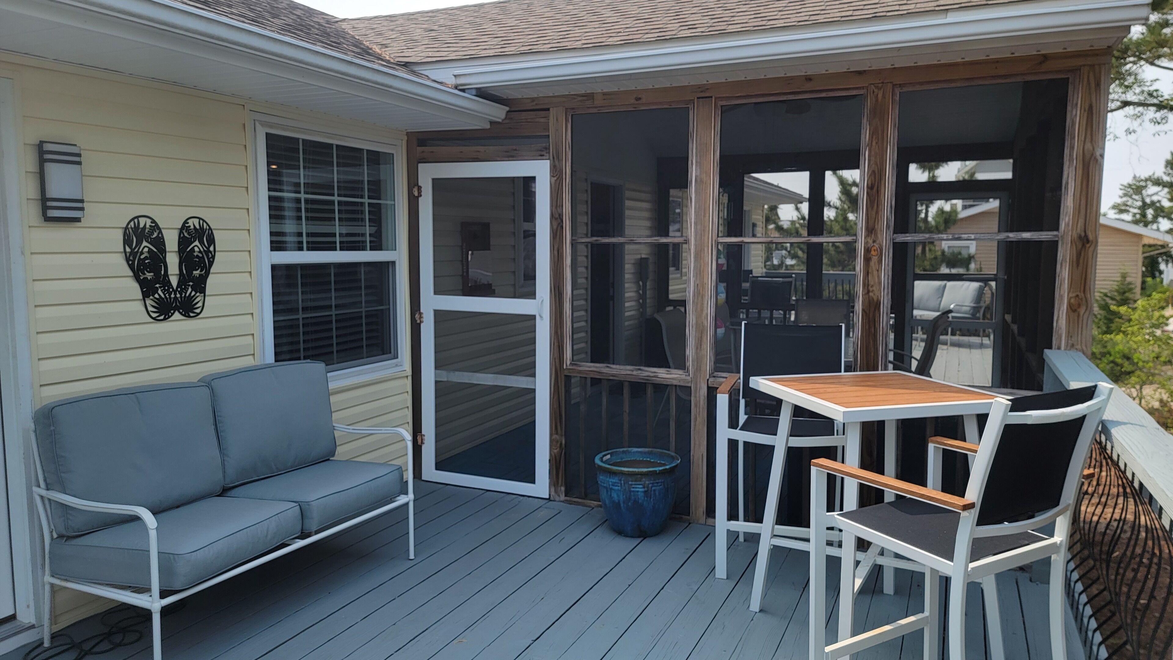 Une terrasse couverte avec un canapé gris, une table en bois et des chaises.