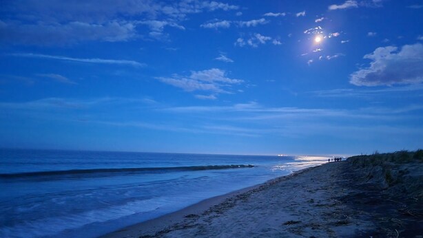 Ein Strand mit blauem Himmel und der Sonne, die am oder über dem Horizont untergeht oder aufgeht.