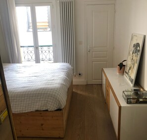A bedroom with a bed, a dresser, a radiator, and a window with curtains. - Bright apartment near the Eiffel Tower (Paris)