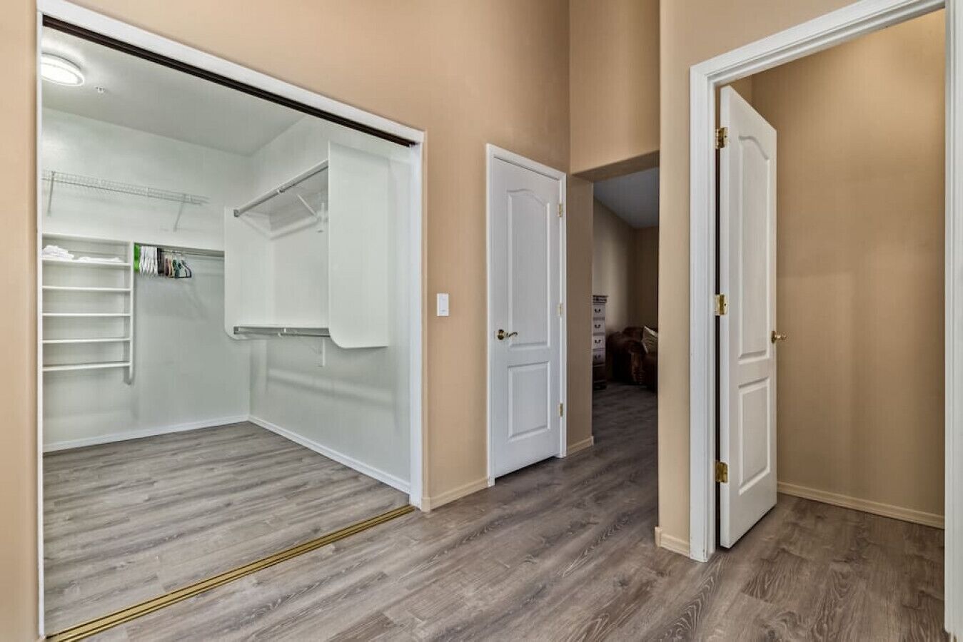 A hallway with a closet, a door leading to another room, and a wooden floor.
