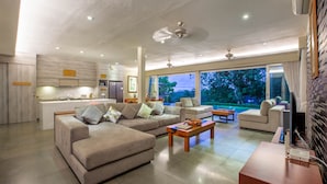 A modern living room with a sofa, coffee table, and a TV. There is a kitchen area with a refrigerator and a dining table. - Luxury 3BR Kahuripan Villa (Bali)