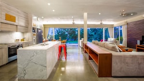 A modern kitchen with a marble island, a red stool, and a large window overlooking greenery. - Luxury 3BR Kahuripan Villa (Bali)