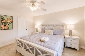 A bedroom with a bed, two bedside tables, a ceiling fan, and a door.