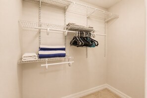 A closet with shelves and hanging rods, containing folded towels and hanging clothes. - Park Shore Resort-1stFloor BLDGJ#154 (Park Shore Resort)