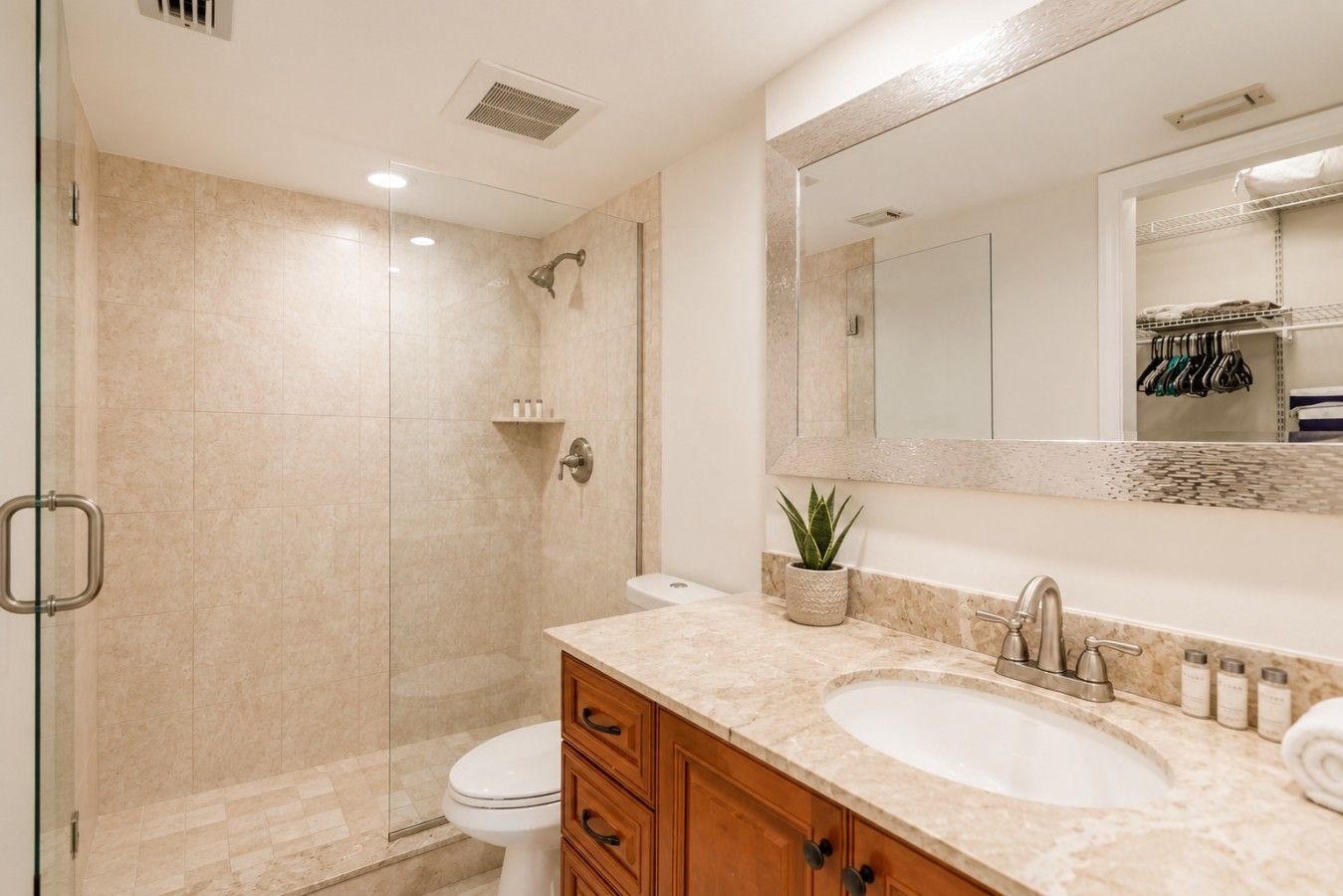 A bathroom with a glass shower enclosure, a white toilet, a vanity with a marble countertop, and a large mirror.