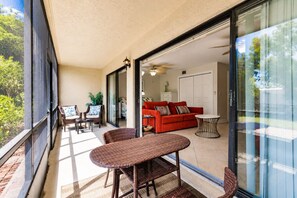 A balcony with wicker furniture, a red sofa, and a glass door leading to an interior space with a ceiling fan.
