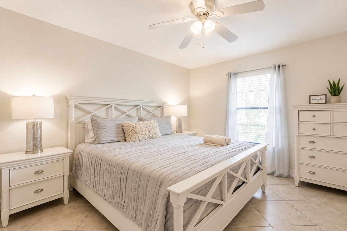 A bedroom with a bed, nightstands, a dresser, a ceiling fan, and a window with curtains.