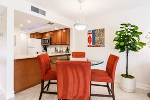 A modern kitchen with wooden cabinets, a central island, and a dining area with red chairs. - Park Shore Resort-1stFloor BLDGJ#154 (Park Shore Resort)
