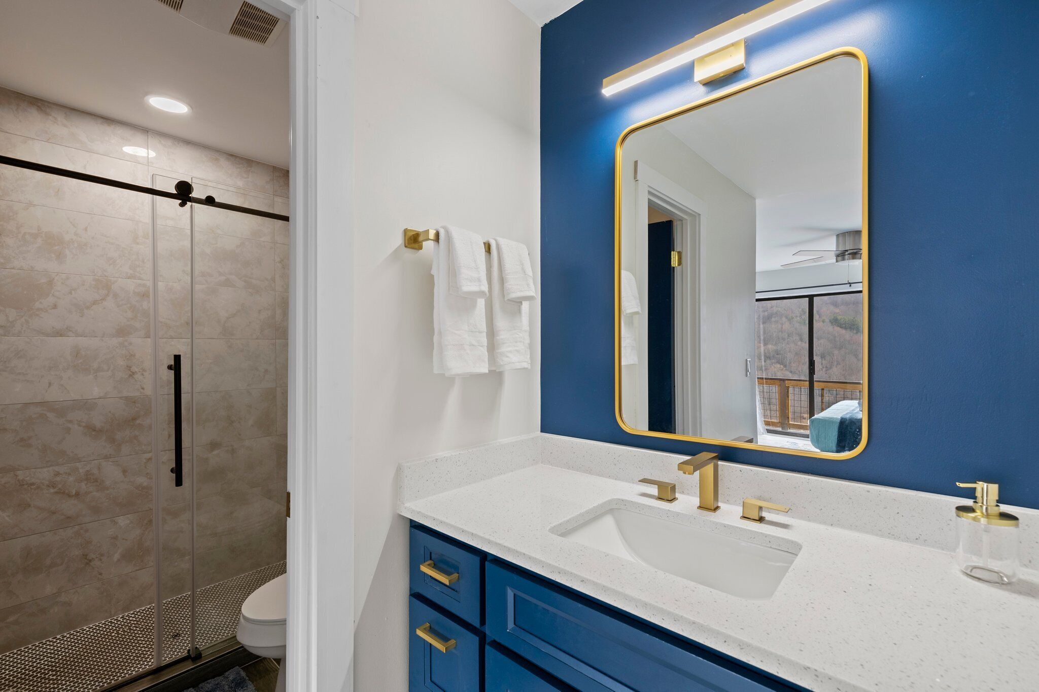 A modern bathroom with a white sink, gold fixtures, a blue accent wall, and a large mirror.