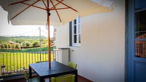 A balcony with a table and chairs, a large umbrella, and a view of a green landscape. - Apartment in an old renovated mill with terrace (Capannori)