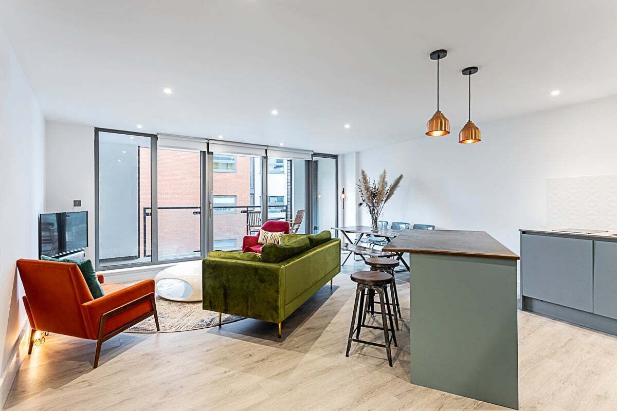 A modern living space with a green sofa, orange armchair, and a kitchen area with a bar stool.