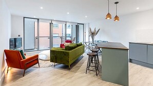 Un espace de vie moderne avec un canapé vert, un fauteuil orange et un coin cuisine doté d’un tabouret de bar.