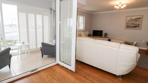 A modern living room with a white sofa, a grey armchair, and a glass door leading to a balcony. - Haul a Gwynt (Holyhead)